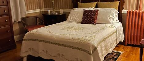 Un dormitorio con una cama con dosel de madera, una mesita de noche con lámpara, una silla, un aparador y un tapete estampado.