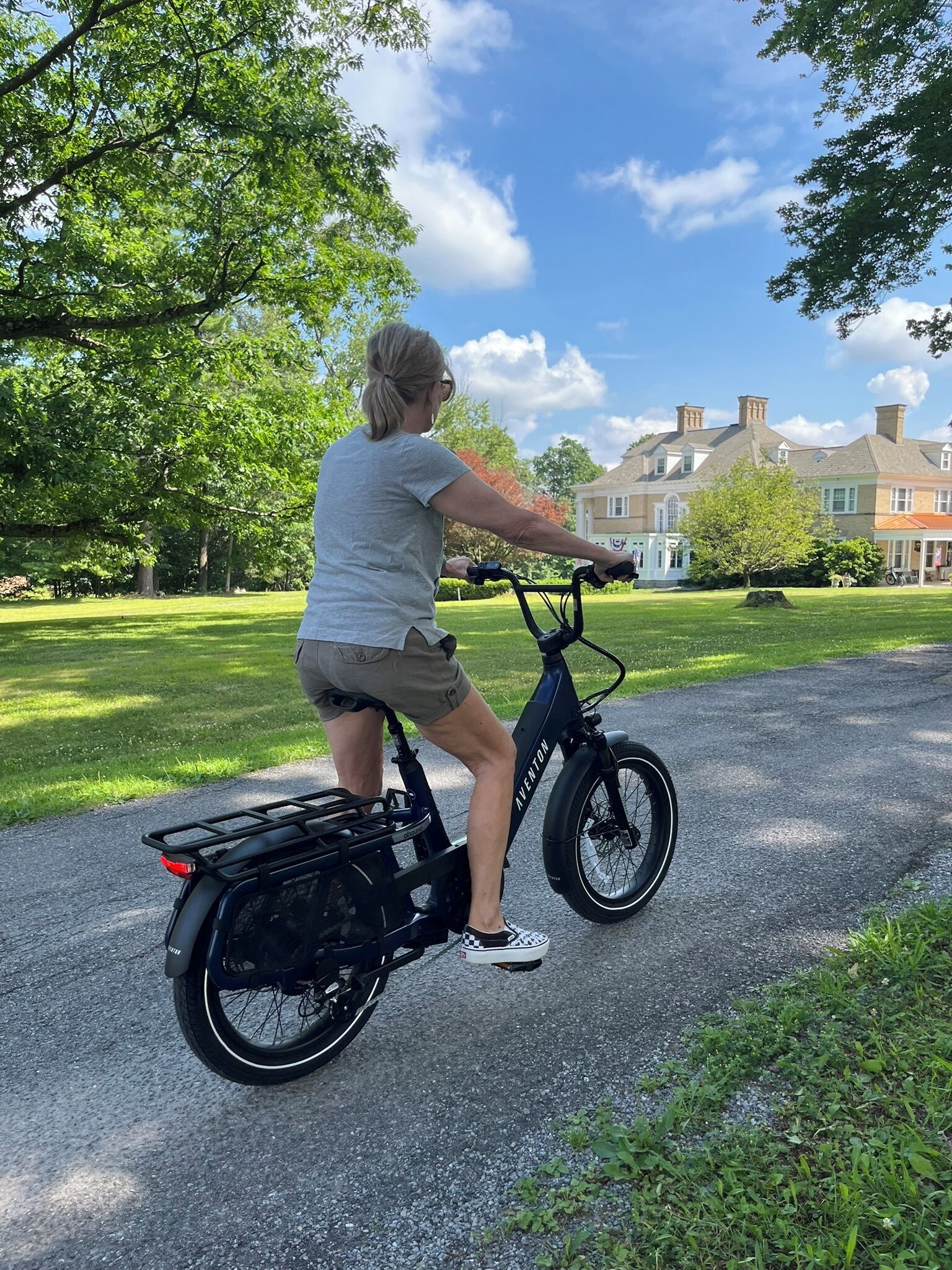 Eine Person fährt ein schwarzes E-Bike auf einem asphaltierten Weg in einem Park mit Gras und Bäumen.