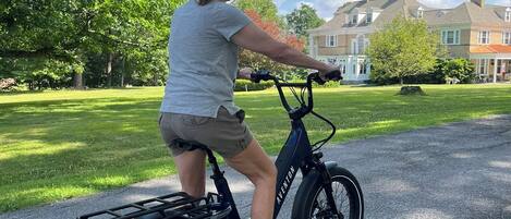 Eine Person fährt ein schwarzes E-Bike auf einem asphaltierten Weg in einem Park mit Gras und Bäumen.