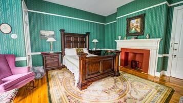 A traditional bedroom with a wooden bed, a fireplace, and green patterned wallpaper.