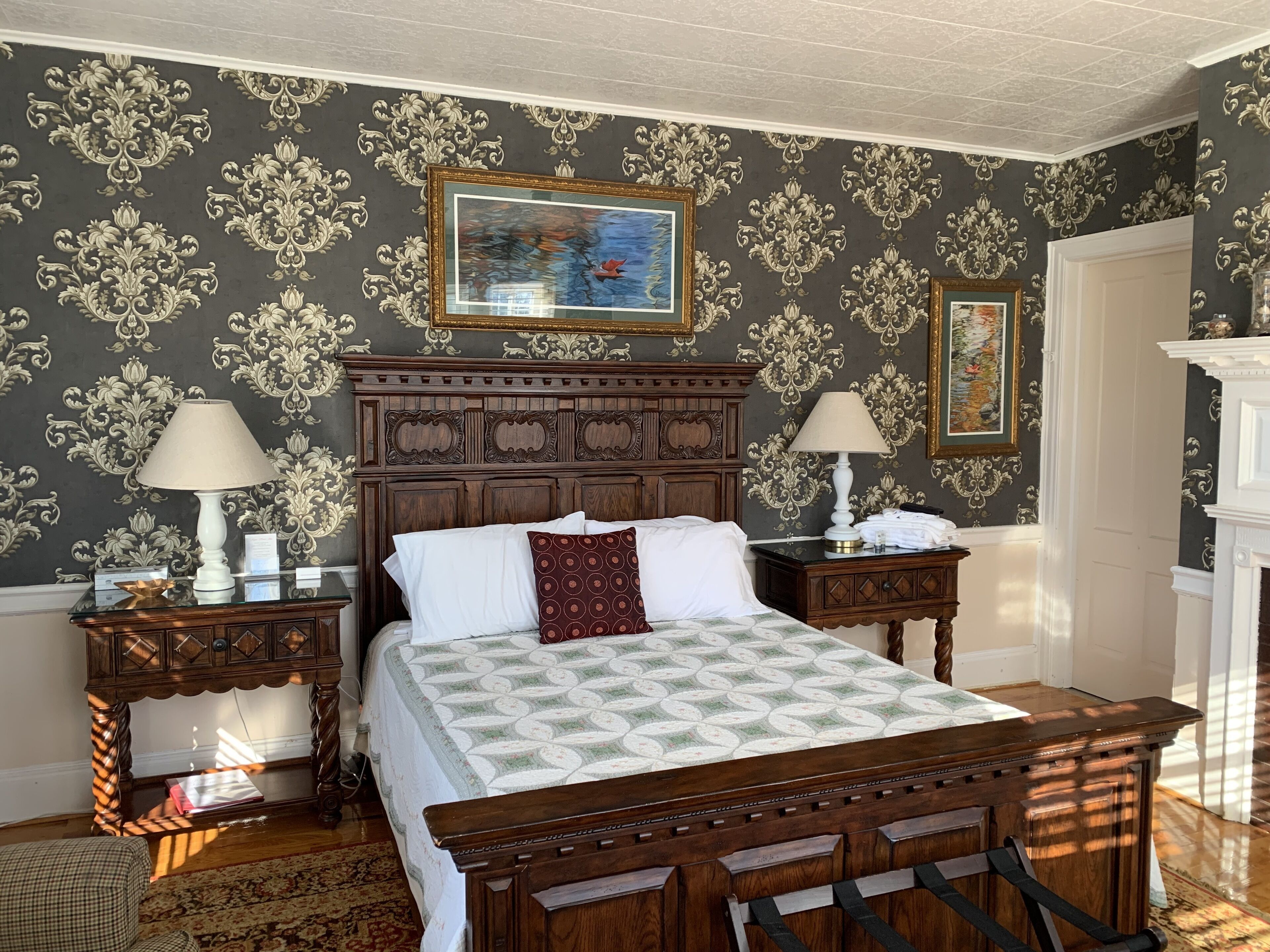 Un dormitorio clásico con una cama de madera grande, papel tapiz decorativo y una chimenea.