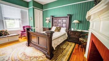 A traditional bedroom with a four-poster bed, a wooden floor, a floral rug, and a green patterned wallpaper.