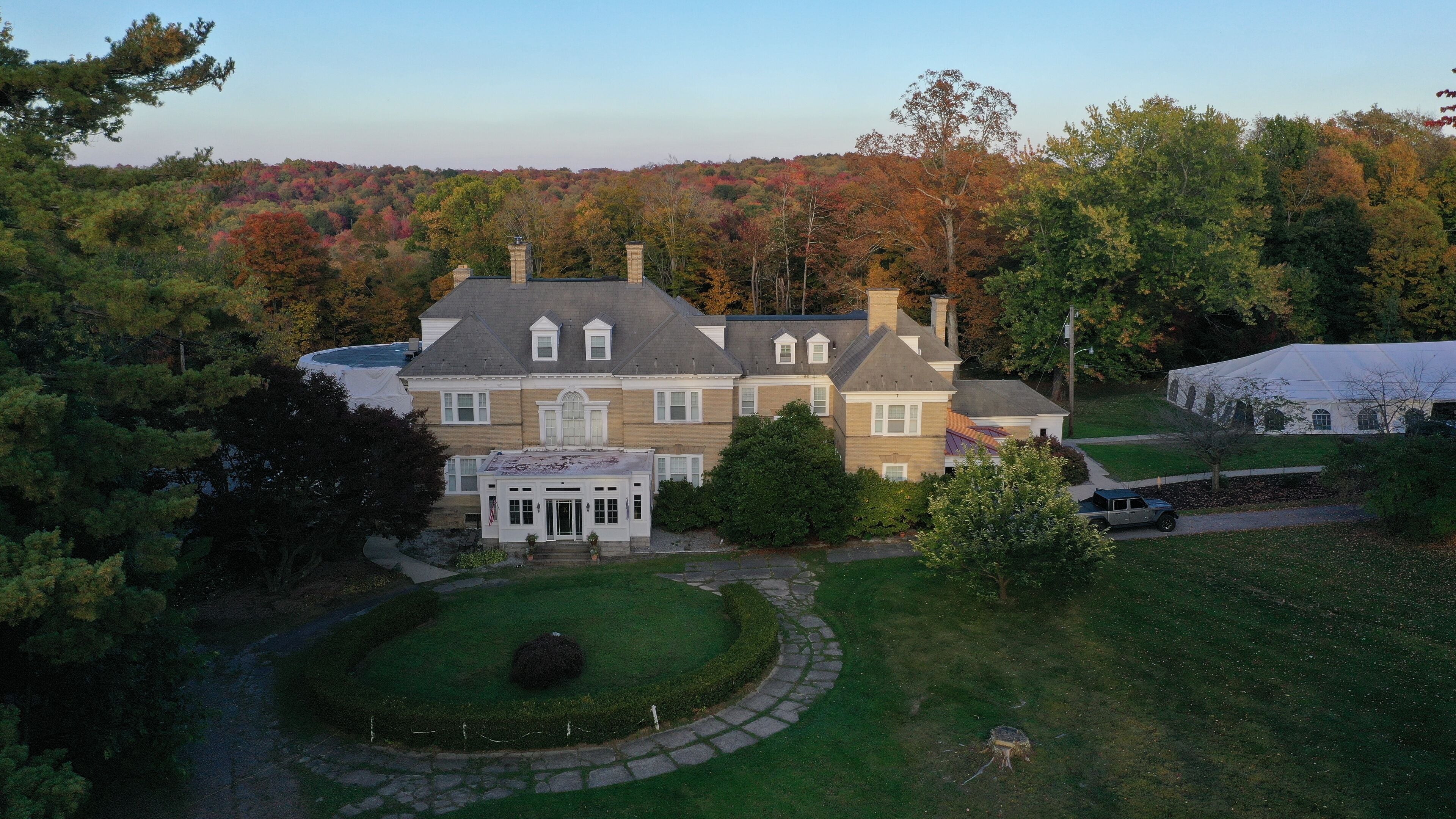 A large, two-story house with a wrap-around porch, a well-maintained lawn, and a view of a forested area.
