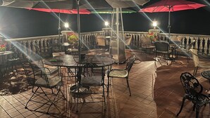 An outdoor patio with round tables and chairs, umbrellas, and a decorative metal structure. - Kane Manor Inn (Kane)