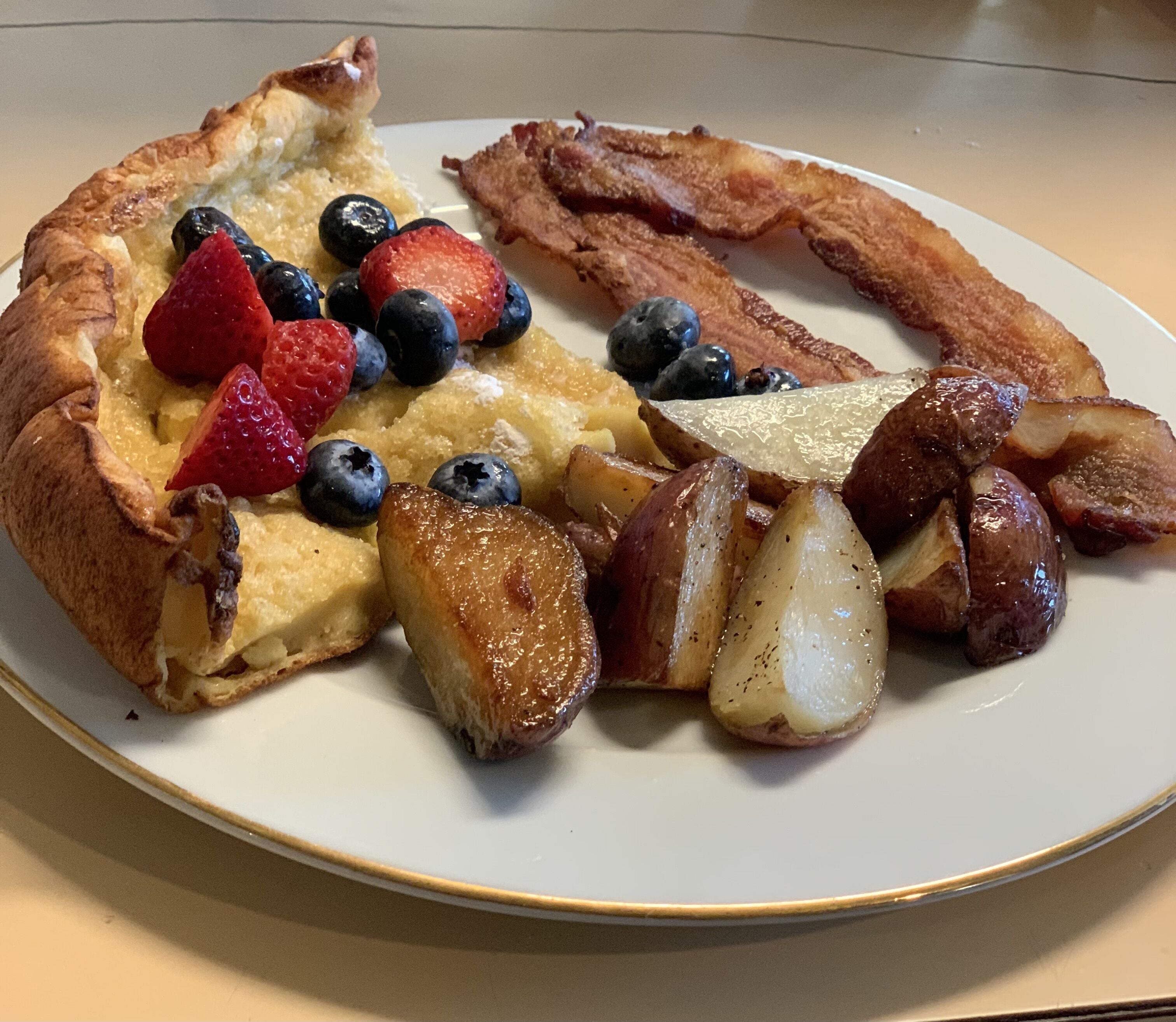 En tallerken med ristet brød, bacon, blåbær, jordbær og ristede kartofler.