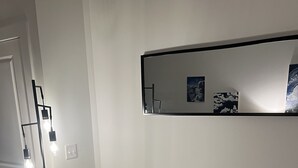 Un salón con un sofá color beige, un cojín que dice 'Reservado para el perro', un espejo montado en la pared y una lámpara.