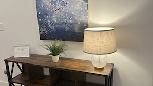 Una consola de madera con una planta en maceta, un cartel enmarcado y una lámpara.