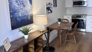 Una cocina moderna con armarios blancos, un microondas y un horno. Hay una mesa de comedor con sillas y una lámpara.