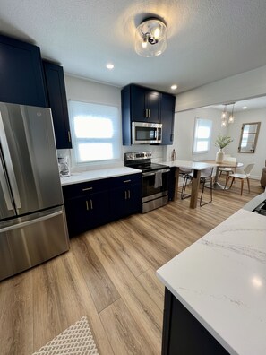Une cuisine moderne avec des meubles bleu foncé, des appareils en acier inoxydable et un plancher en bois.