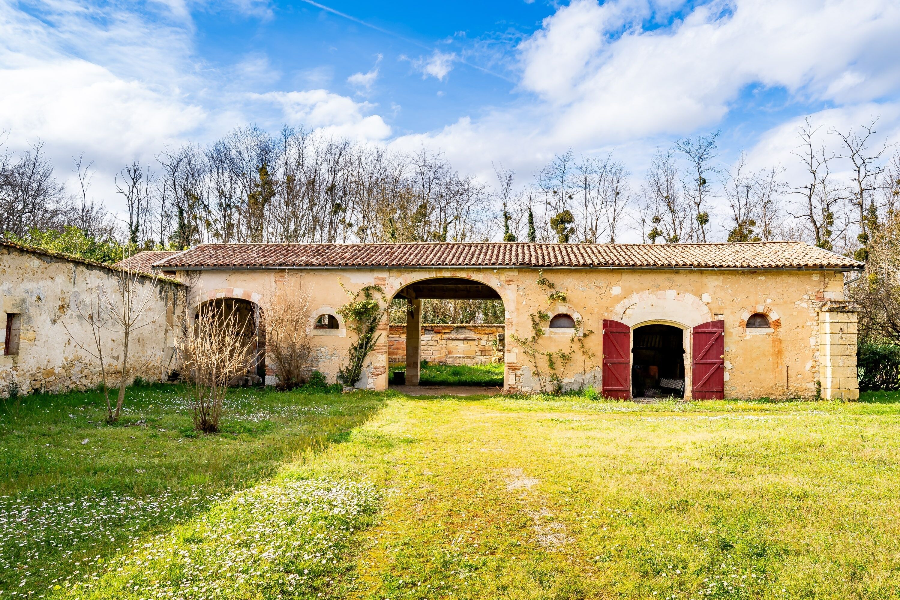 An old building with a tiled roof, arched doorways, and a grassy courtyard.