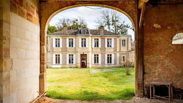 Un arco de entrada que conduce a un patio con un edificio al fondo.