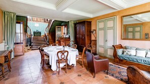 Un comedor con una mesa dispuesta para cuatro personas, sillas de madera, un sofá y una escalera que sube a un nivel superior.