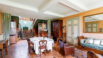 Un espace repas avec une table dressée pour quatre personnes, des chaises en bois, un canapé et un escalier menant à un niveau supérieur.