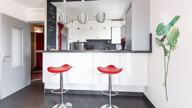Een moderne keuken met witte kasten, een zwart aanrecht en twee rode barkrukken.
