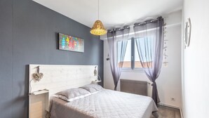 Een slaapkamer met een bed, nachtkastje, wandplank, plafondlamp, raam met gordijnen en een radiator.