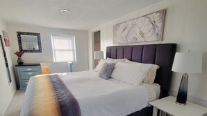 Un dormitorio ordenado con una cama grande, mesitas de noche, un aparador y una ventana.