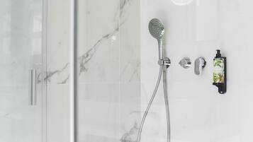 A modern shower with a handheld showerhead, a wall-mounted control, and a soap dispenser.