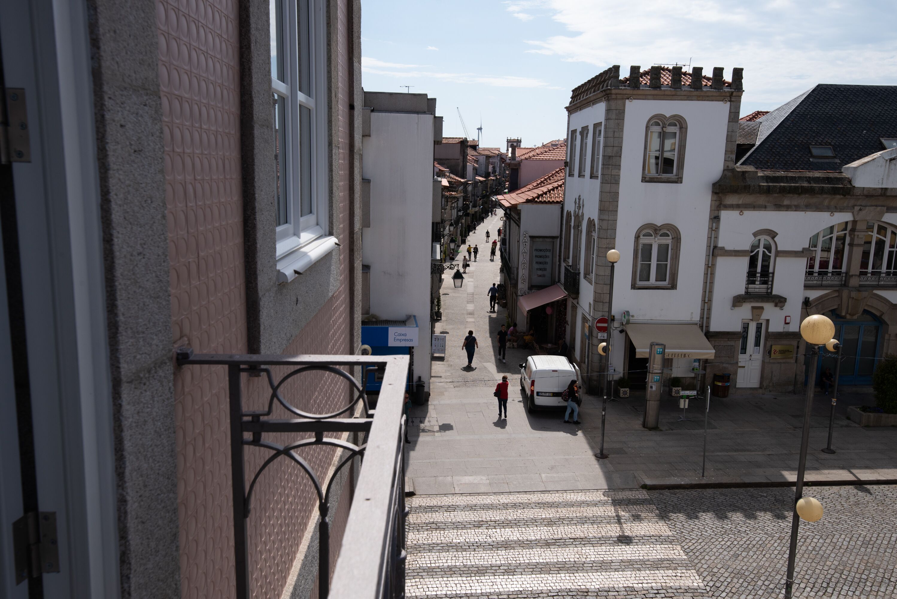 Una calle estrecha flanqueada por edificios, una furgoneta blanca estacionada a la derecha y algunos peatones.