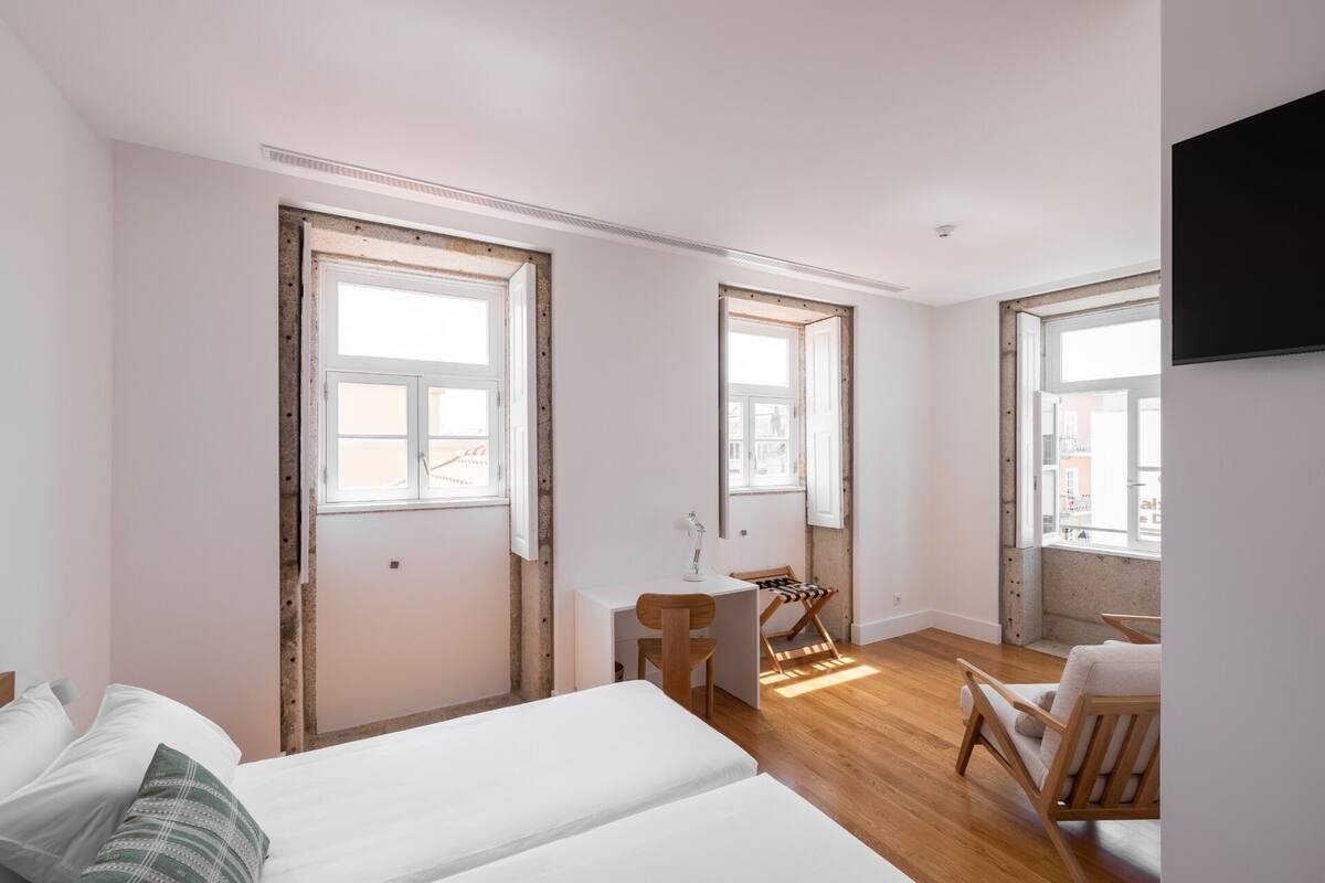 Un dormitorio con cama, escritorio, silla y dos ventanas.