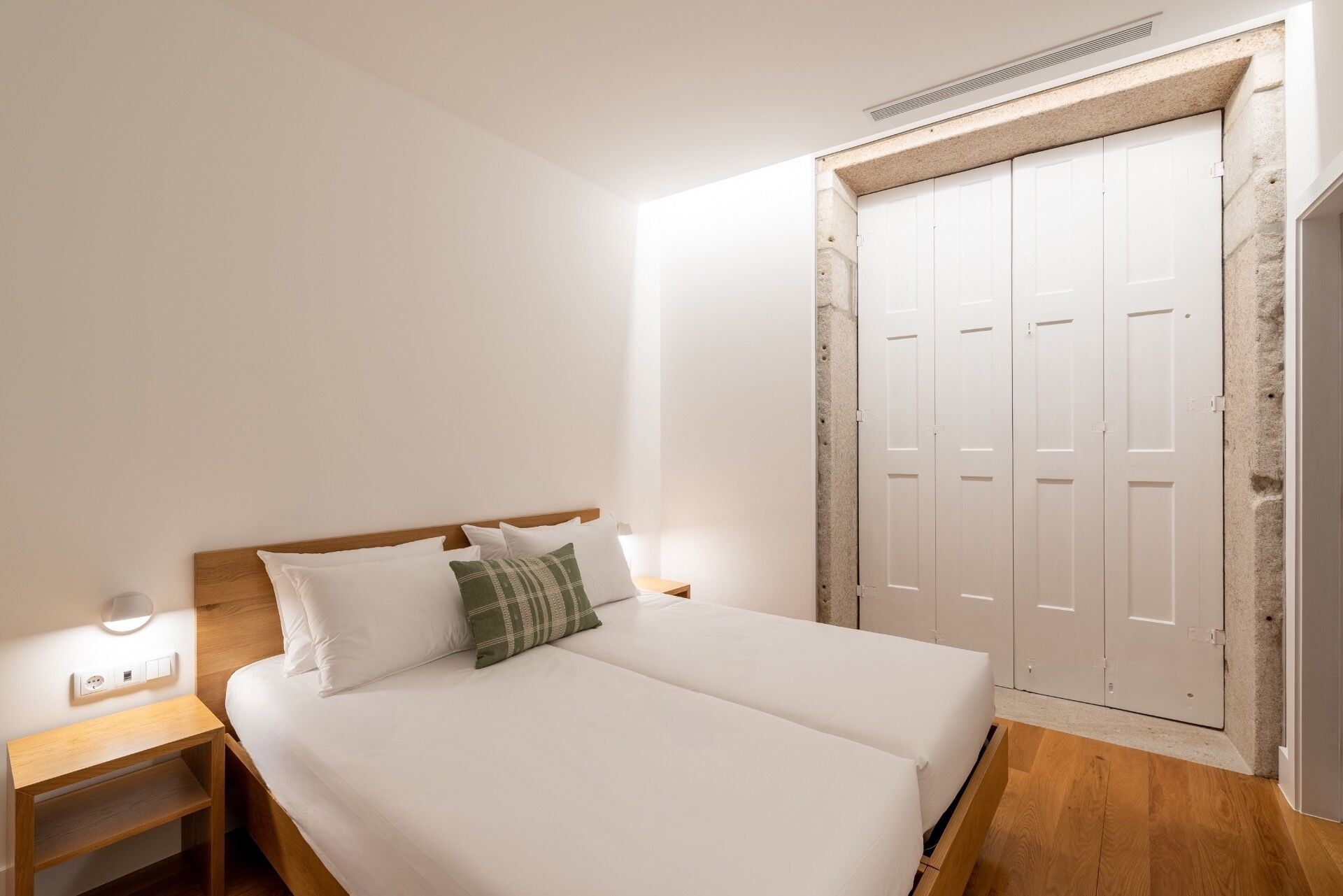 A bedroom with a bed, a nightstand, a wall-mounted light, and a closet with a stone accent wall.