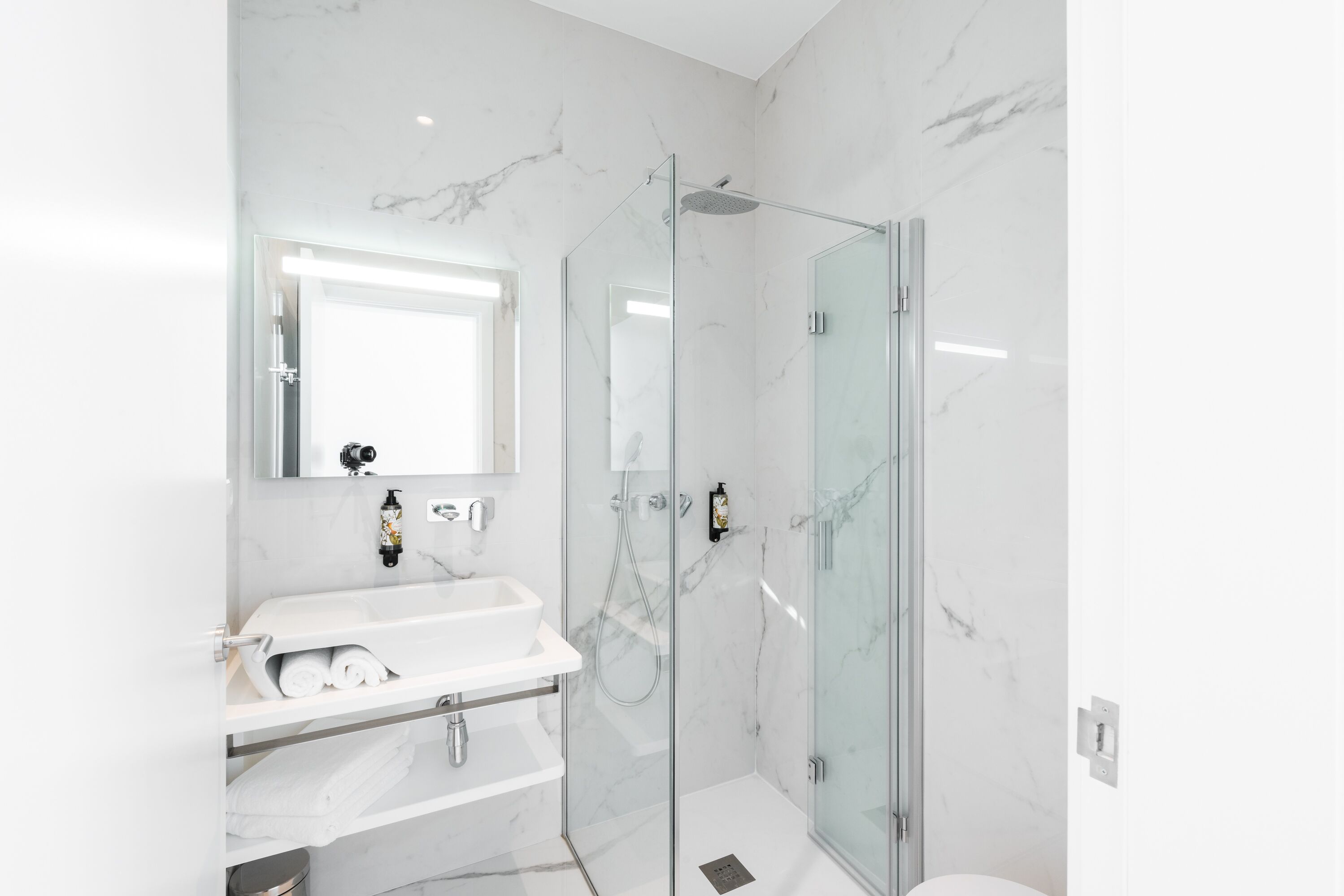 Un baño moderno con ducha de vidrio, lavamanos de mármol blanco y un espejo grande.
