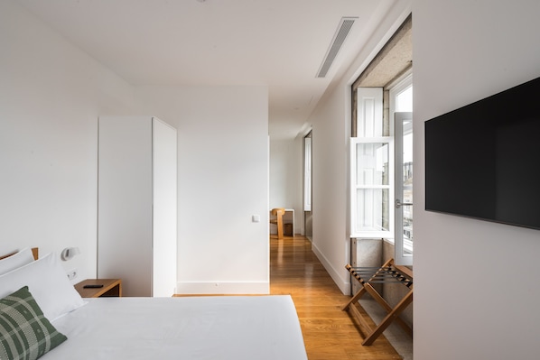 Habitación de hotel moderna con una cama grande, un televisor montado en la pared y vistas a la ciudad a través de amplios ventanales.