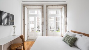 Un dormitorio con cama, escritorio y silla. Dos puertas dan acceso a un balcón.