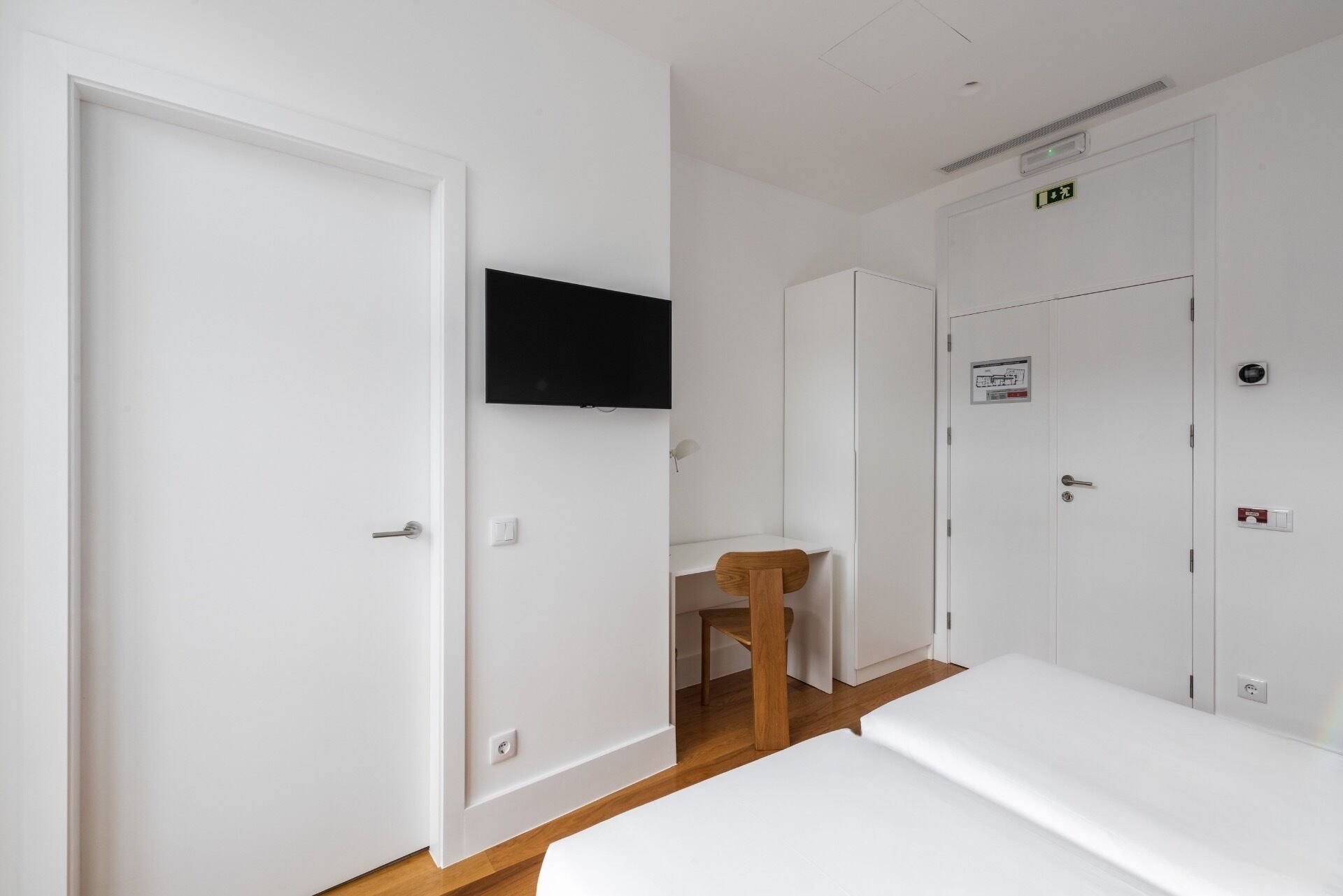 A hotel room with a bed, a desk, a chair, and a TV mounted on the wall.