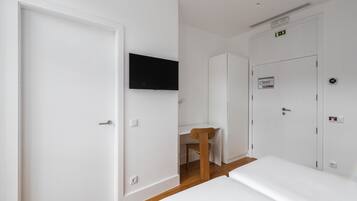 A hotel room with a bed, a desk, a chair, and a TV mounted on the wall.