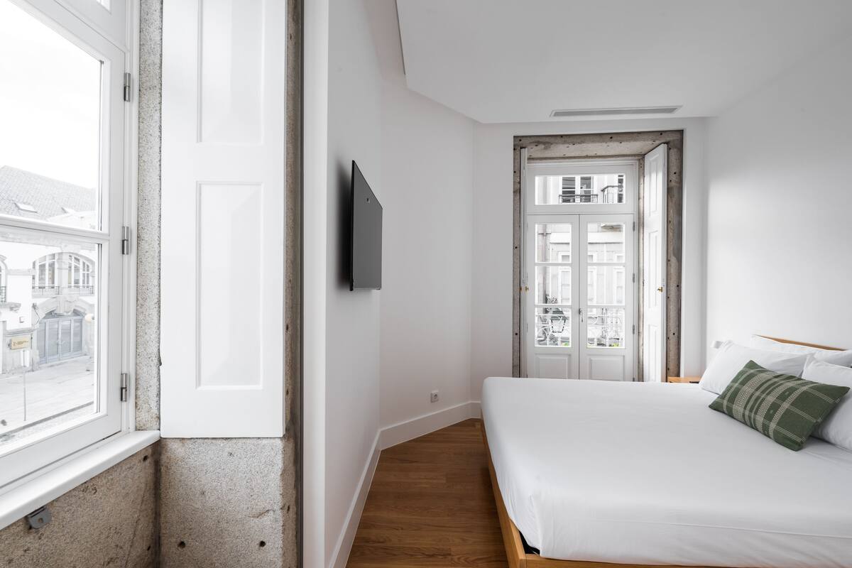 Un dormitorio con una cama de madera, un televisor blanco montado en la pared y una puerta que da a un espacio al aire libre.