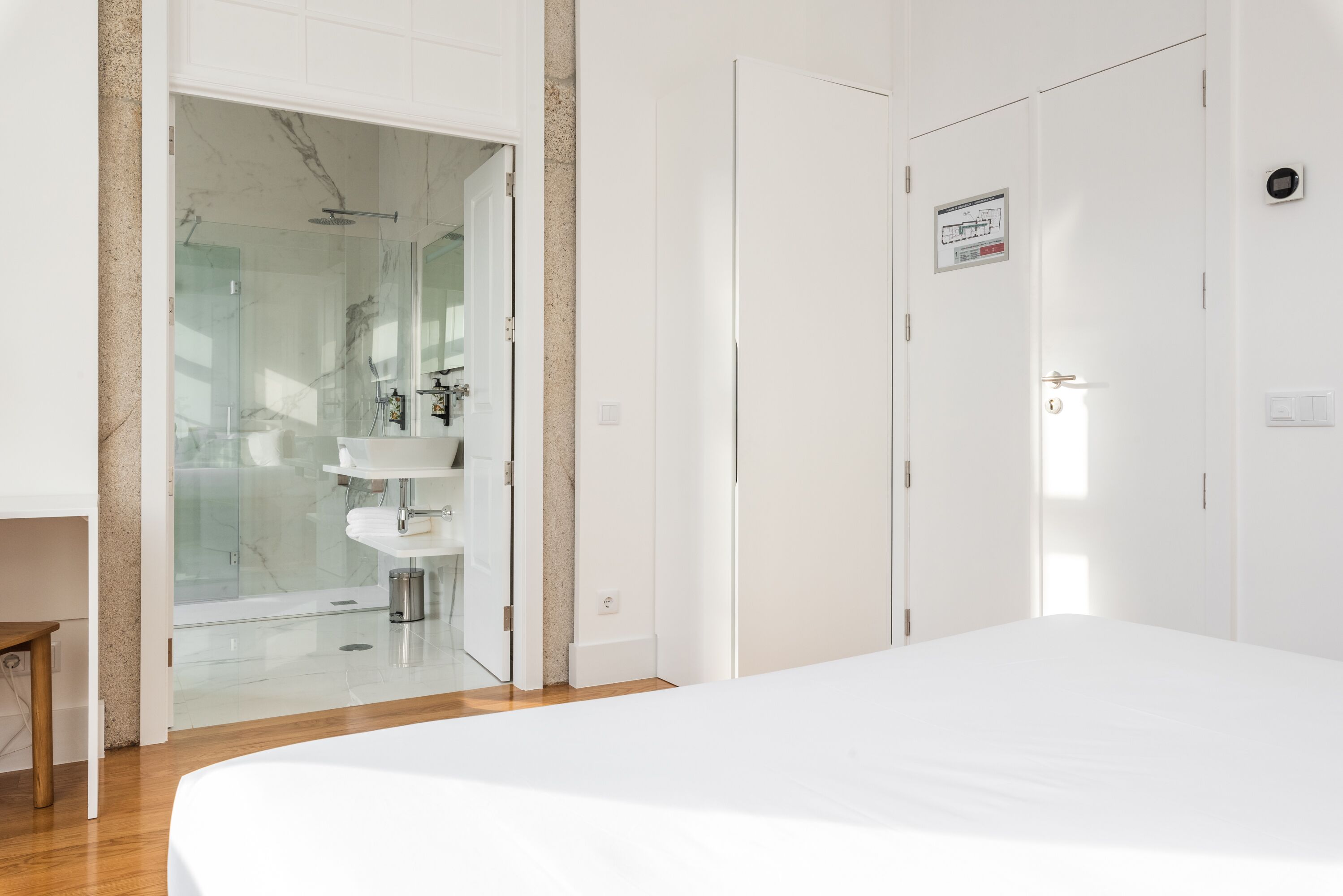 A modern bedroom with a large bed, a glass shower enclosure, and white wardrobes.