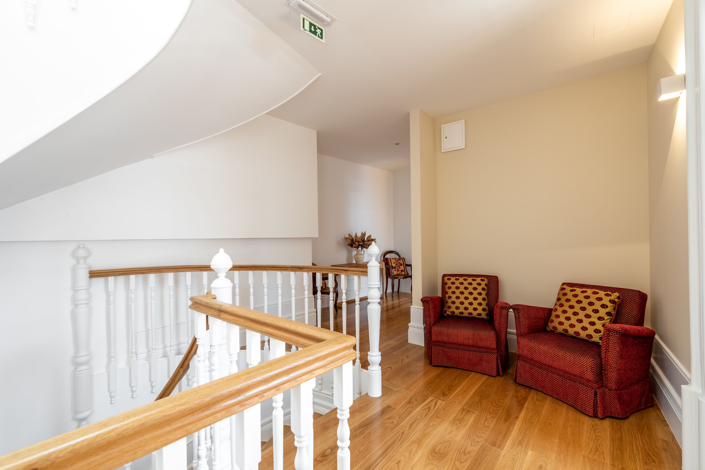 A spacious hallway with a wooden staircase, a red armchair, and a beige wall.