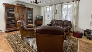 Un salon avec un canapé en cuir marron, un meuble en bois, une télévision et un tapis à motifs.