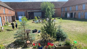 Une cour avec une scène, des sièges en plein air et un jardin agrémenté de plantes et de fleurs en pot.