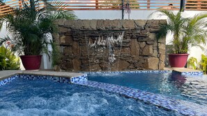 Una piscina con una cascada de piedra, rodeada de plantas en macetas.