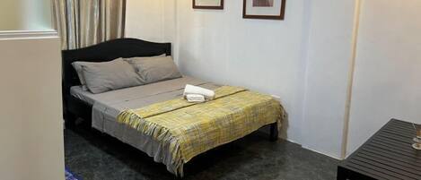 Quarto pequeno e bem arrumado com uma cama, uma mesa e duas imagens emolduradas na parede.