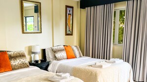 Habitación de hotel con dos camas, una mesita de noche, una lámpara y una ventana con cortinas.