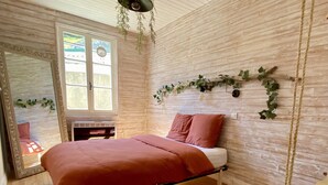 Un dormitorio con cama, una planta colgante, un espejo y una ventana.