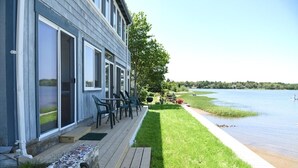 Una casa con terraza que da a un lago, con un césped y mobiliario de exterior.