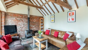 A cozy living room with a brick wall, wooden beams, a fireplace, leather sofas, and a television. - 5 bedroom accommodation in Thorpe Culvert, near Skegness (Thorpe Culvert, near Skegness)