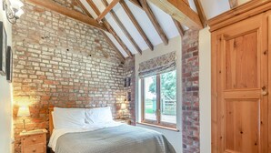 A bedroom with a brick wall, wooden beams, a bed with white linens, a wooden wardrobe, and a window with a view of the outdoors. - 5 bedroom accommodation in Thorpe Culvert, near Skegness (Thorpe Culvert, near Skegness)