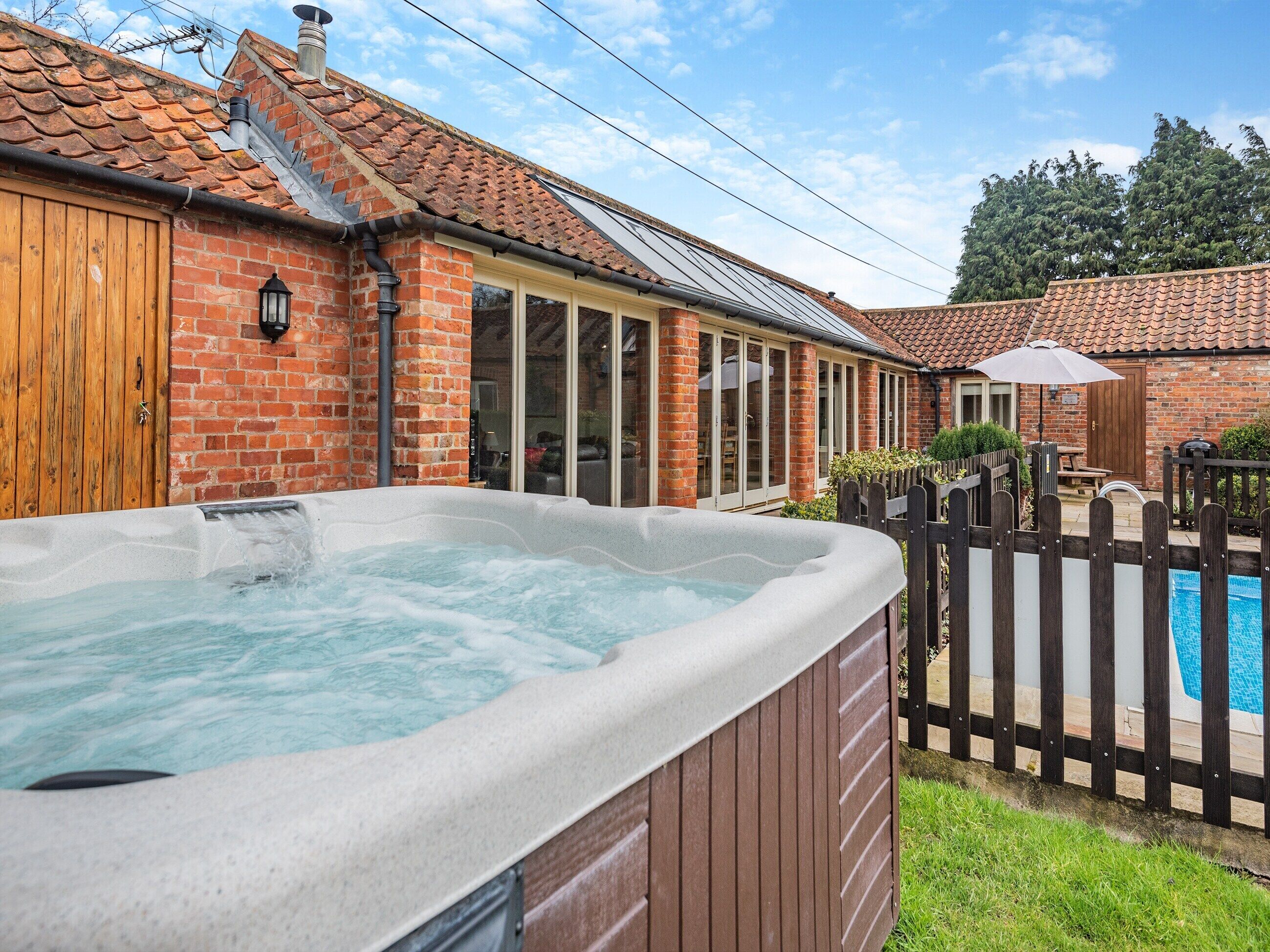 Een hottub in een achtertuin met een huis van baksteen, een houten hek en een zwembad.