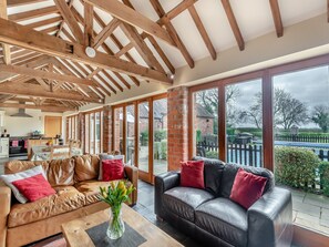 A spacious living area with a high ceiling, wooden beams, a large window, and a view of the outside.