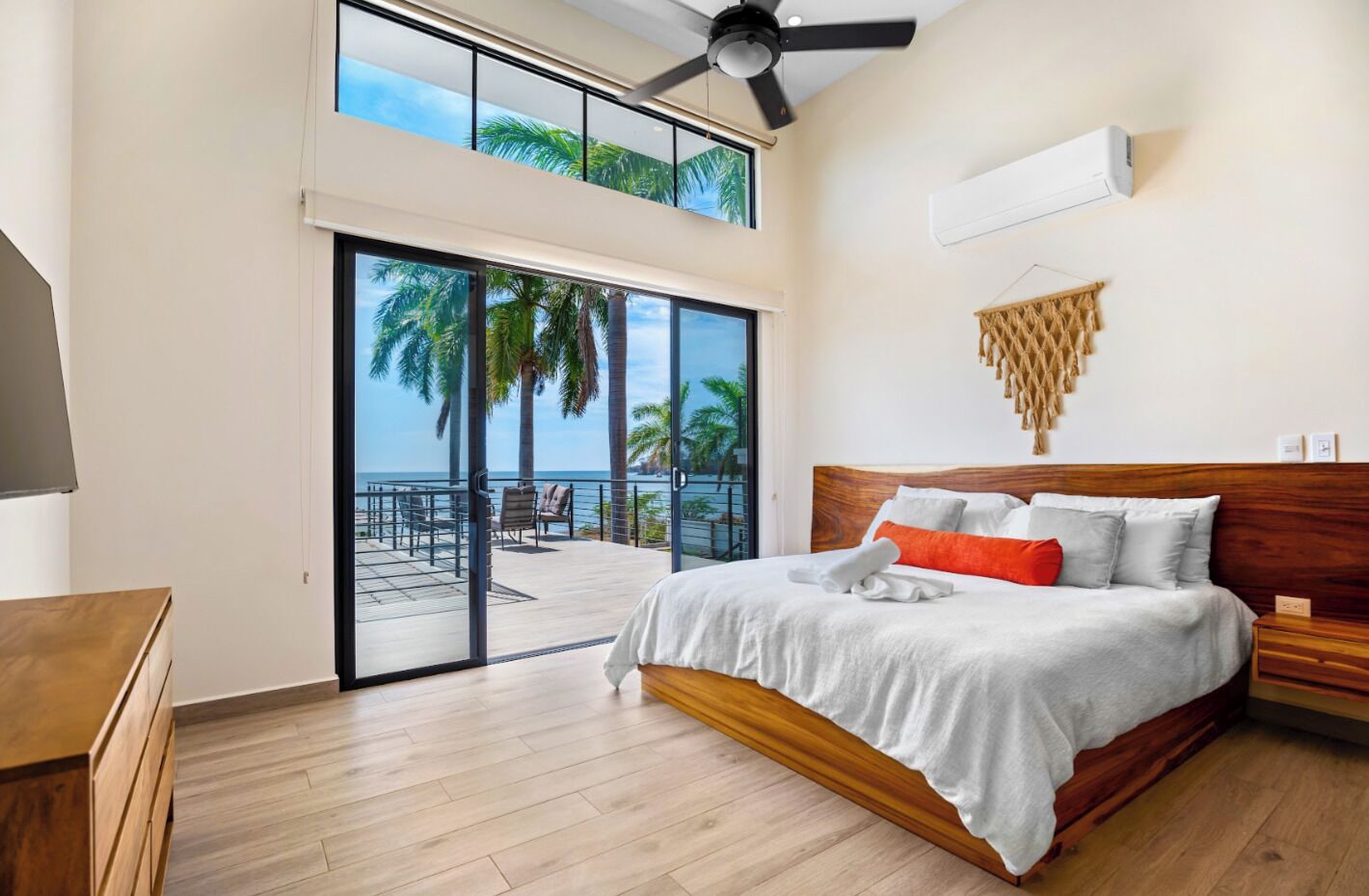 Un dormitorio con una cama grande, un ventilador de techo y vista al océano a través de una puerta corrediza de vidrio.