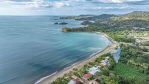 Una zona costera con playa, casas y abundante vegetación.