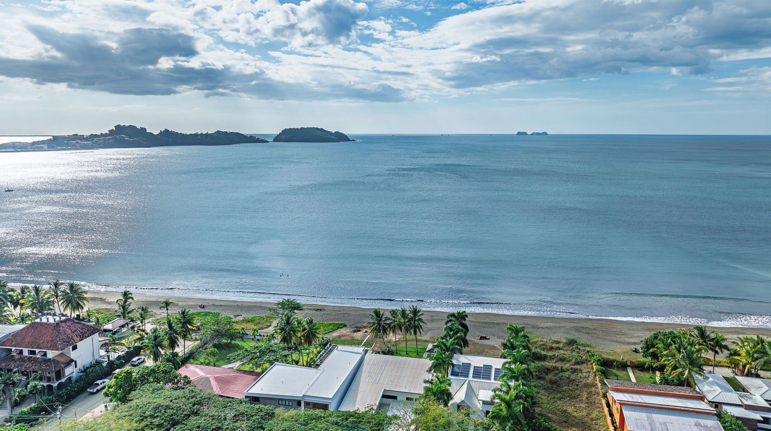 A coastal view with a beach, palm trees, and a distant island.