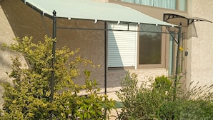 Et hus med en overdækket terrasse, plantekasser og et vindue med persienner.