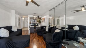 A modern living room with black sofas, a glass coffee table, and a ceiling fan. - Bello condominio con vista al mar, jacuzzi interno y una ubicación privilegiada (Galveston)