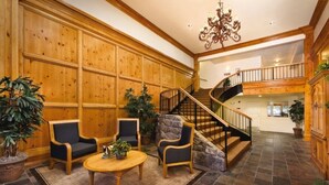 Een ruime lobby met een wand van houten panelen, een accentwand van steen, een ronde houten salontafel, twee rieten fauteuils, en een trap naar een hoger niveau.