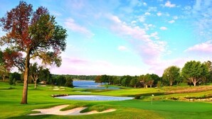 Een golfbaan met zandbunkers, een waterhindernis en een vlag.